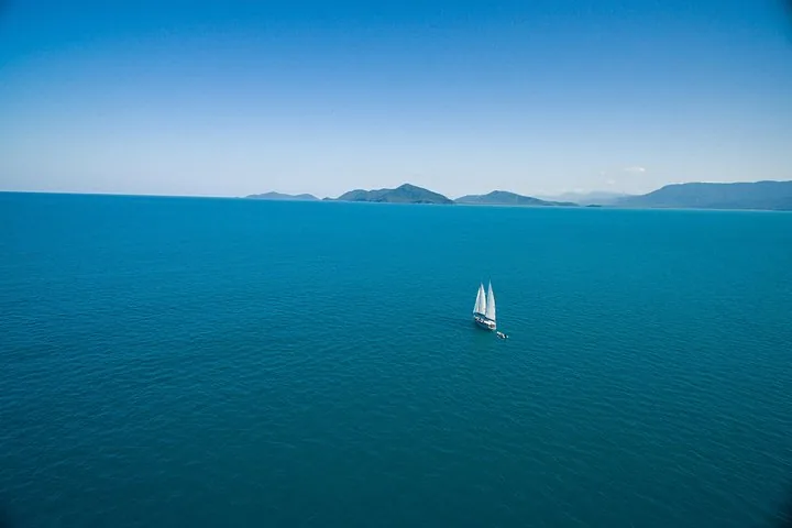 Aerial view of a sailboat sailing on bright blue water near the coast